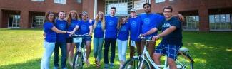 A group of undergraduate orientation leaders pose in matching blue shirts in front of dorms outside on the Biddeford校园